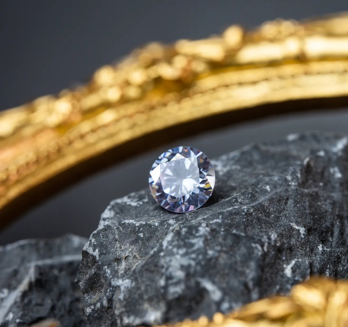 Loose round diamond on dark stone beside a gold ring